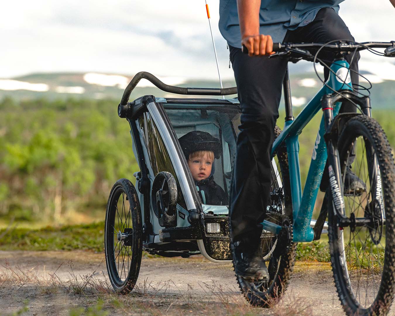 Ett barn som sitter I en cykelvagn från Thule medans en vuxen person cyklar